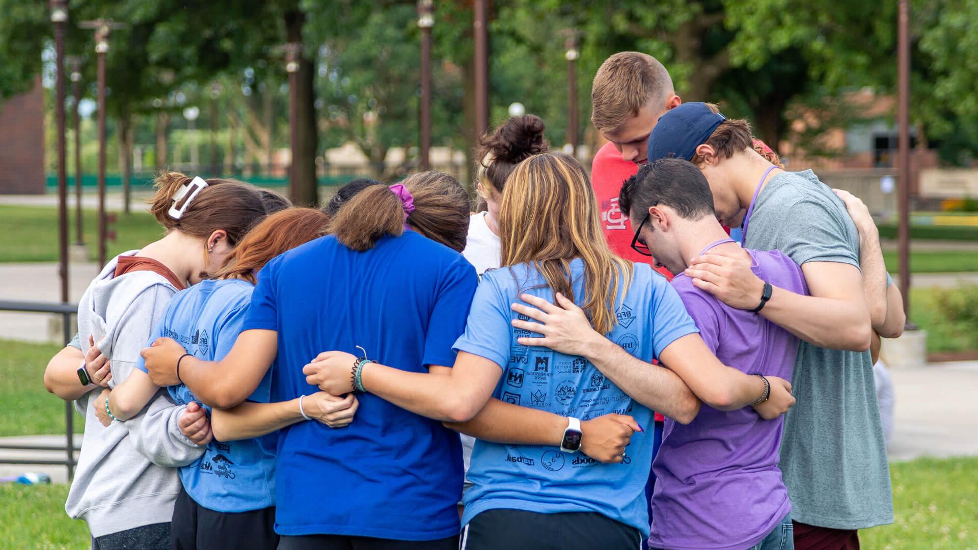 students gather in huddle with arms around each other and heads bowed in prayer